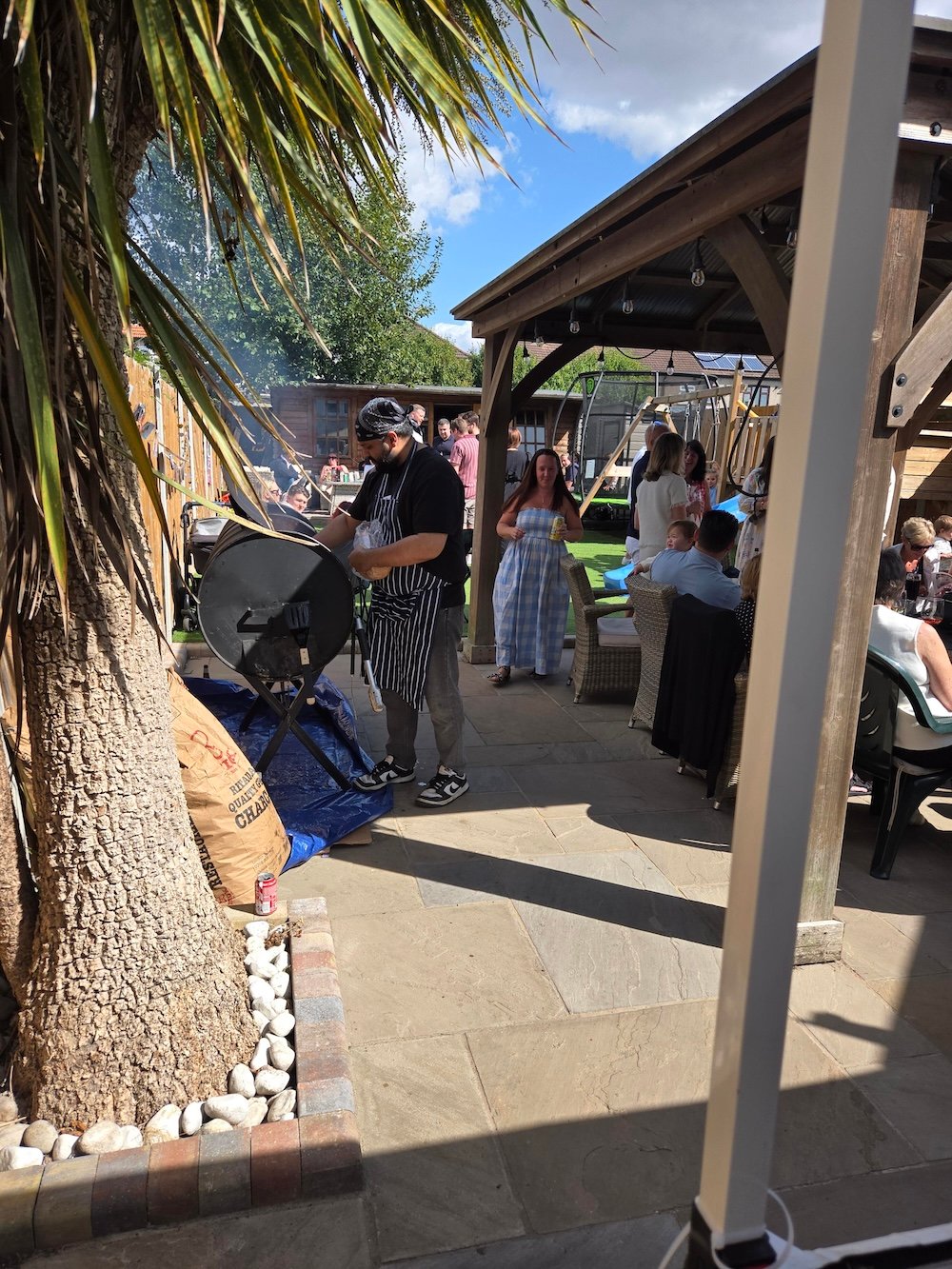 Chef cooking beside an outdoor smoker at a garden gathering