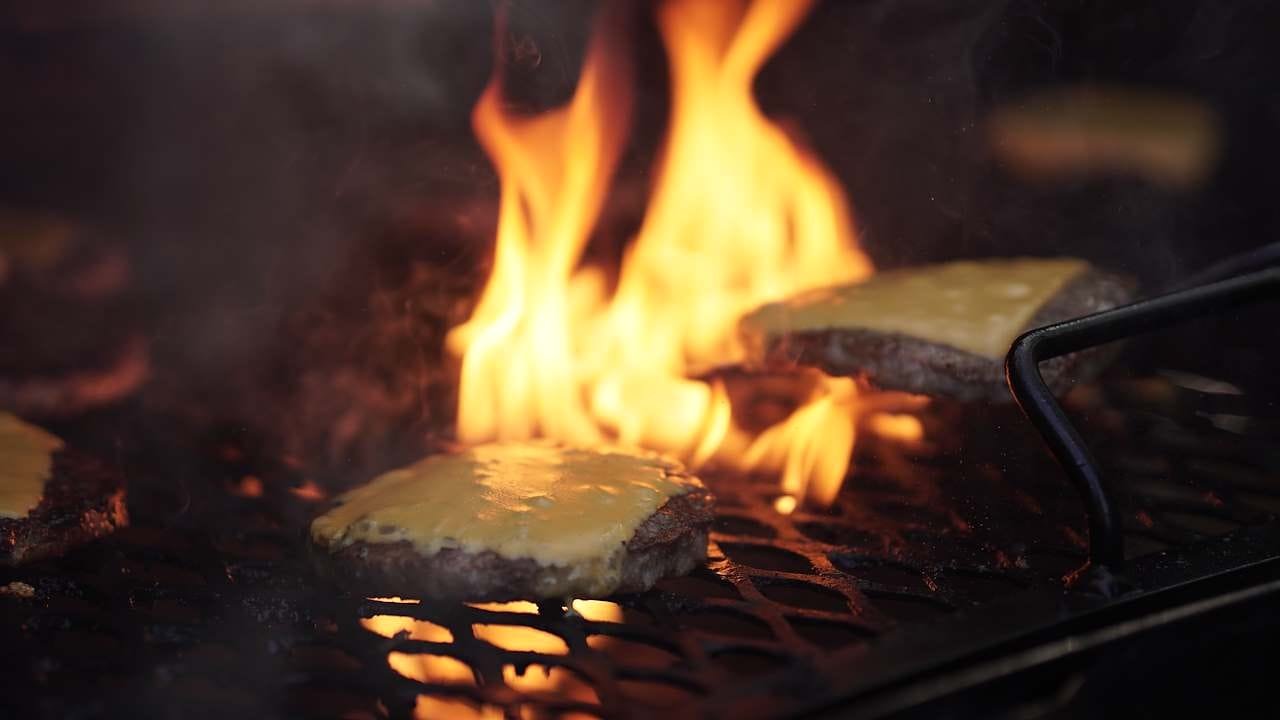 Cheese-topped burger patties cooking over open flames on a barbecue grill